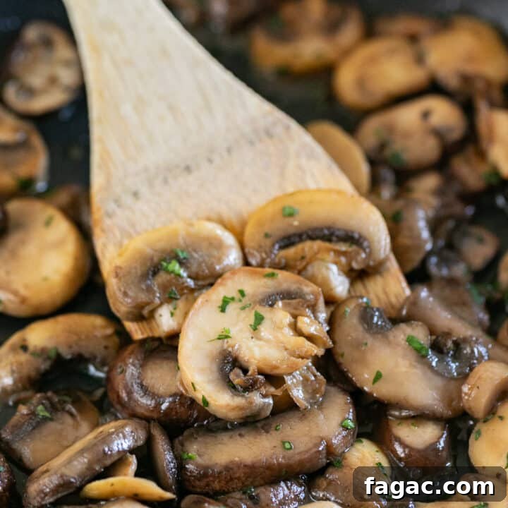A wooden spoon in a pan of sauteed mushrooms.