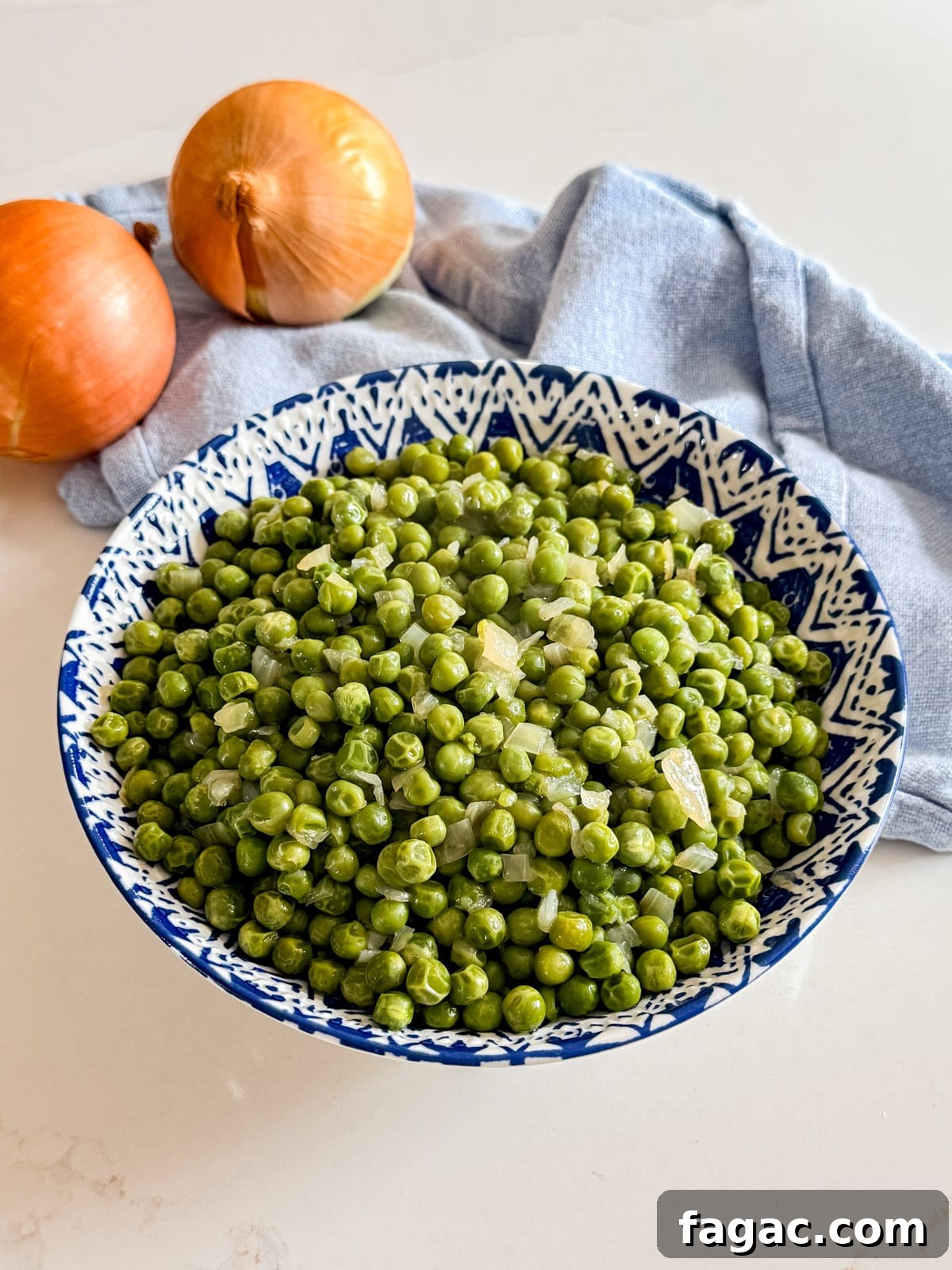 Creamy Garlic Green Peas with Parmesan 8 A bowl of peas with onions and a napkin in the background.
