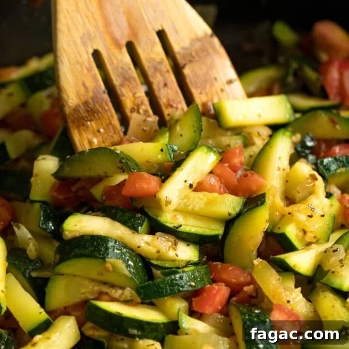 A wooden spoon stirring a pan of zucchini and tomatoes.