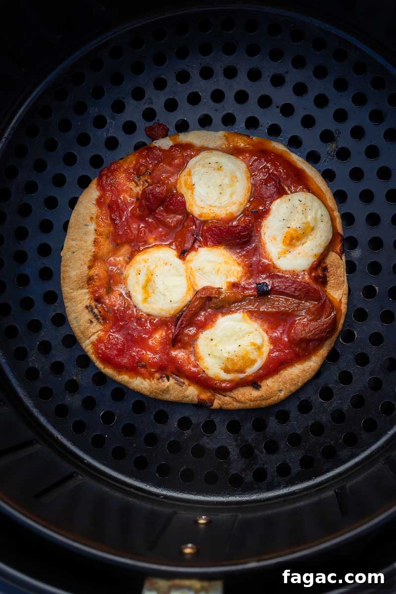Reheat Pizza in an Air Fryer for Extra-Crispy Slices 3 Overhead of a small round pizza cooked in an air fryer with melted mozzarella cheese on top.