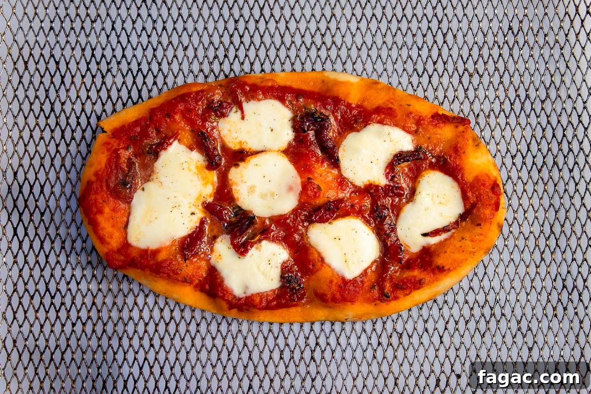 Reheat Pizza in an Air Fryer for Extra-Crispy Slices 4 Overhead view of a small pizza in a large air fryer basket with mozzarella cheese and sundried tomatoes on top.