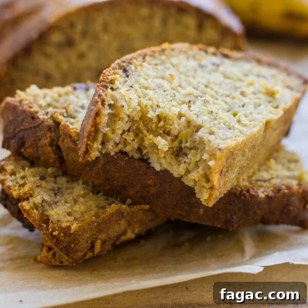 A small stack of slices of air fryer banana bread on a wooden board with the rest of the bread and a banana behind.