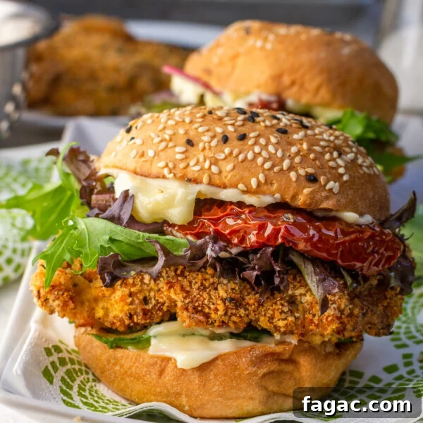 A closeup of an air fryer crispy chicken burger on a green and white patterned napkin and rectangular white plate with another burger in the background.