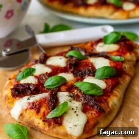 Naan pizza with mozzarella and fresh basil leaves on brown paper and a wooden board with a pizza cutter, colorful salad bowl and more pizza in the background.