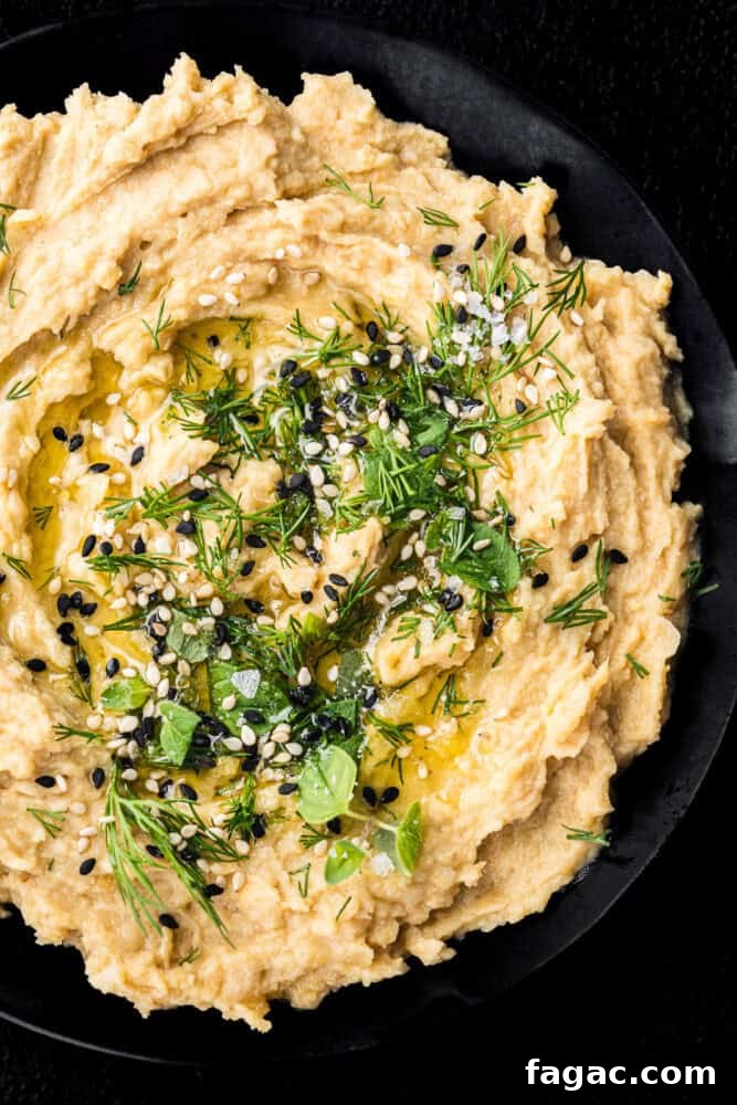 Overhead shot of hummus without tahini in a black bowl, topped with fresh dill, sesame seeds, olive oil, and flaky sea salt.