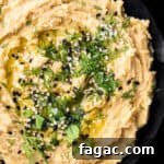 Overhead shot of hummus without tahini in a black bowl, topped with fresh dill, sesame seeds, olive oil, and flaky sea salt.