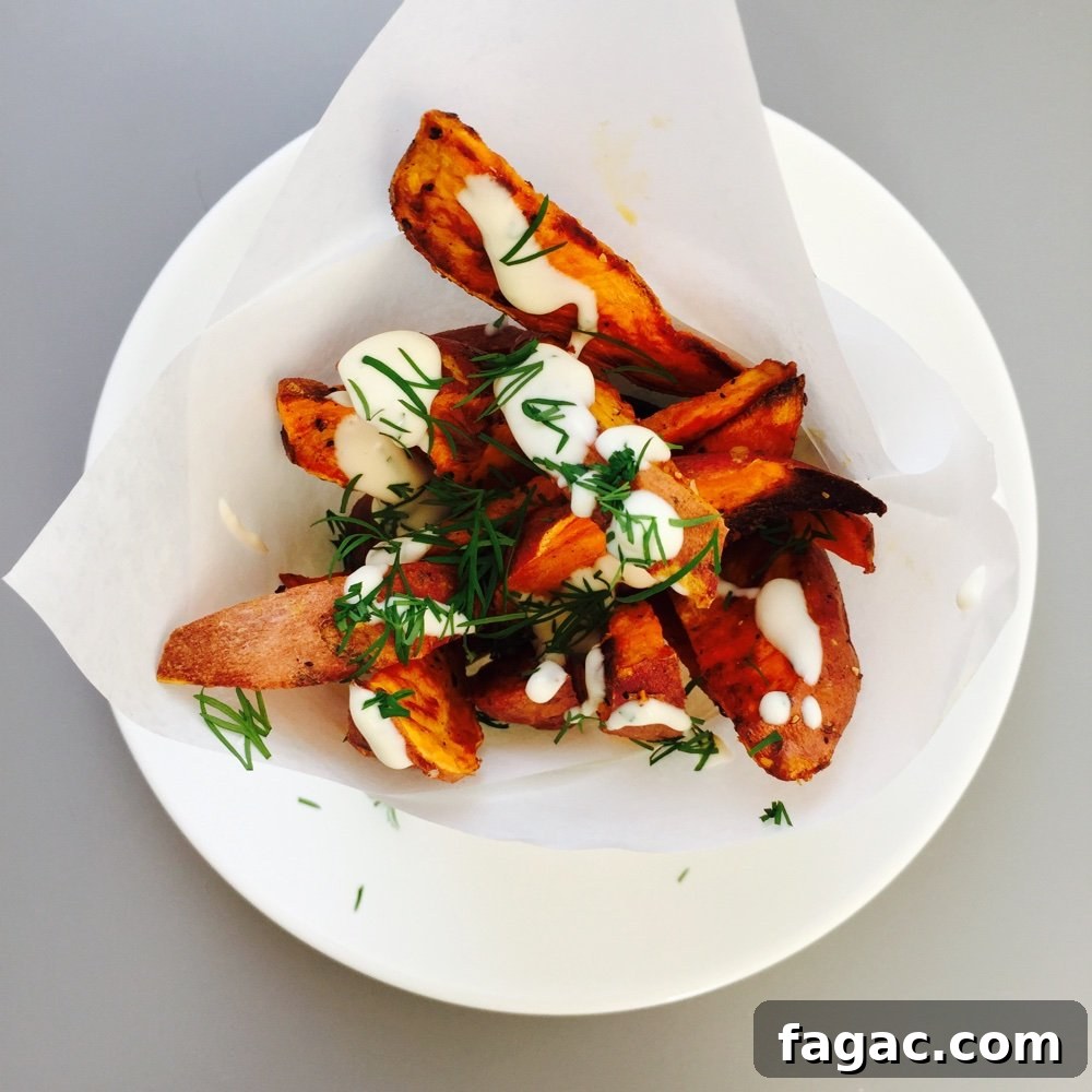 a paper cone of sweet potato wedges with lemon-y mayonnaise drizzled over them and chopped dill scattered over.