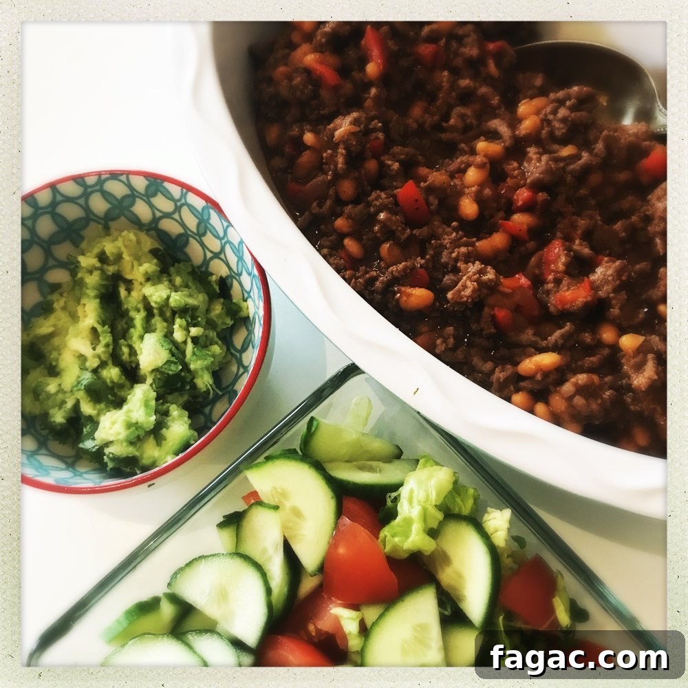 bowl of 20 minute beef and baked bean chilli alongside homemade guacamole and green salad