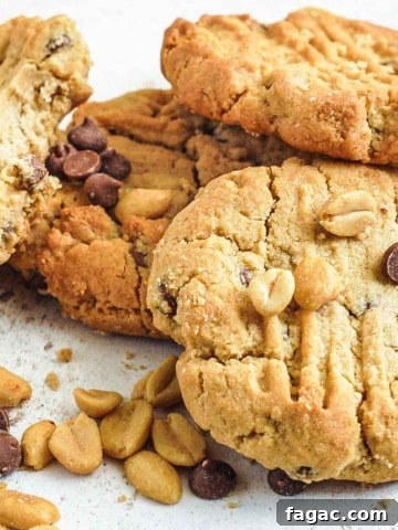 Peanut butter chocolate chip cookies piled onto each other with scatterings for peanuts and chocolate chips