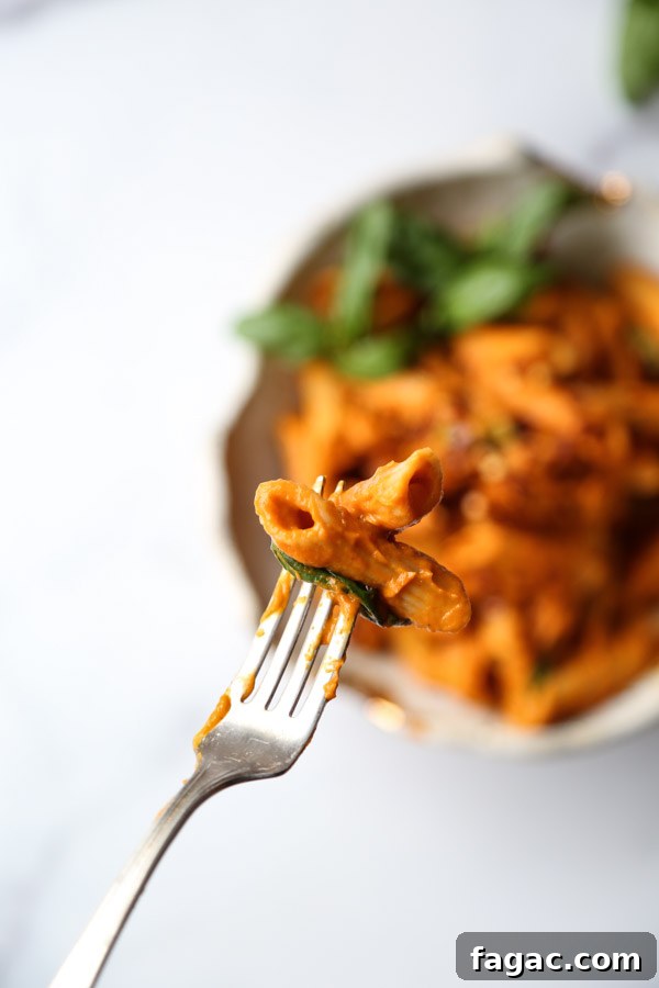 Gluten-Free penne covered low FODMAP pasta sauce in a bowl with fork and two penne in foreground