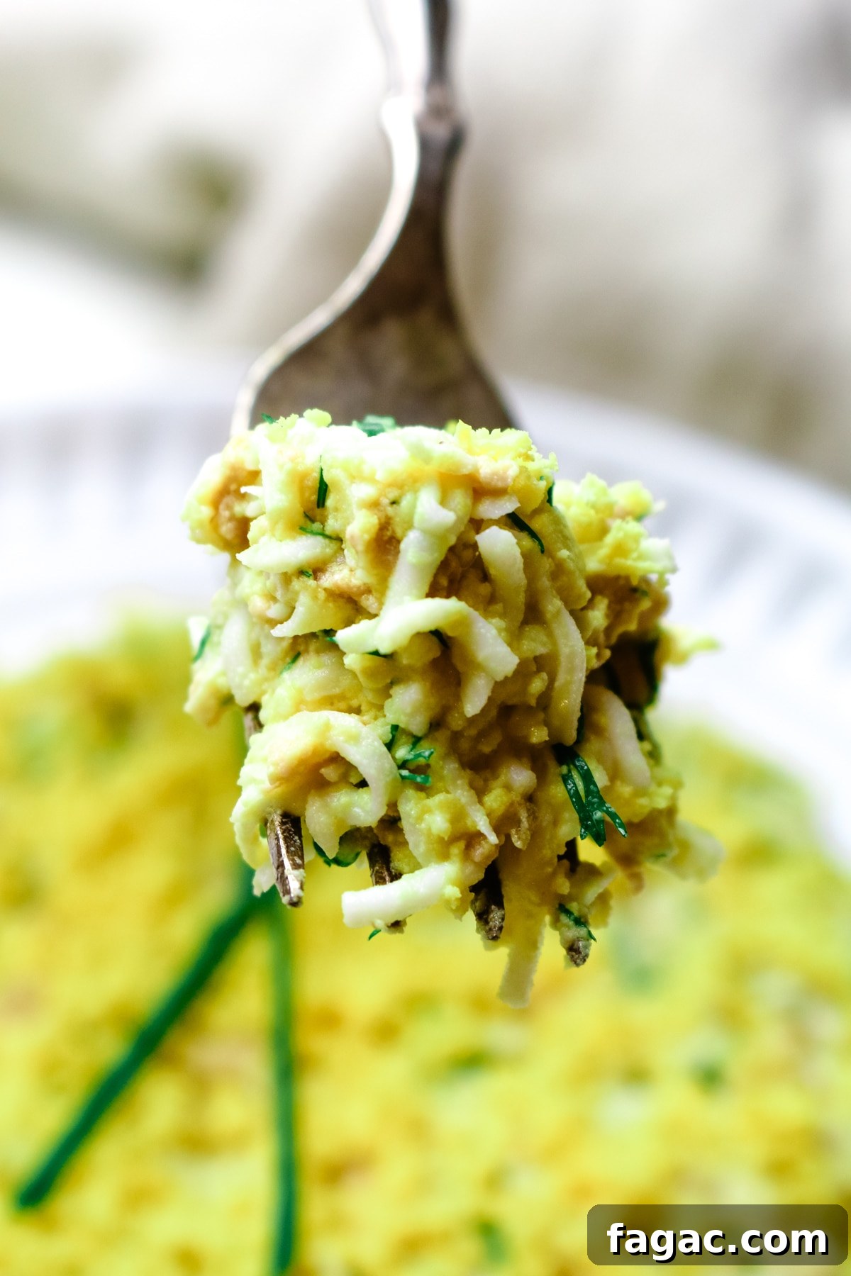 Cod Liver and Egg Salad Recipe: Creamy, Tangy Seafood Salad 11 a bite of cod liver salad with eggs and green onions on a fork with plate in background.