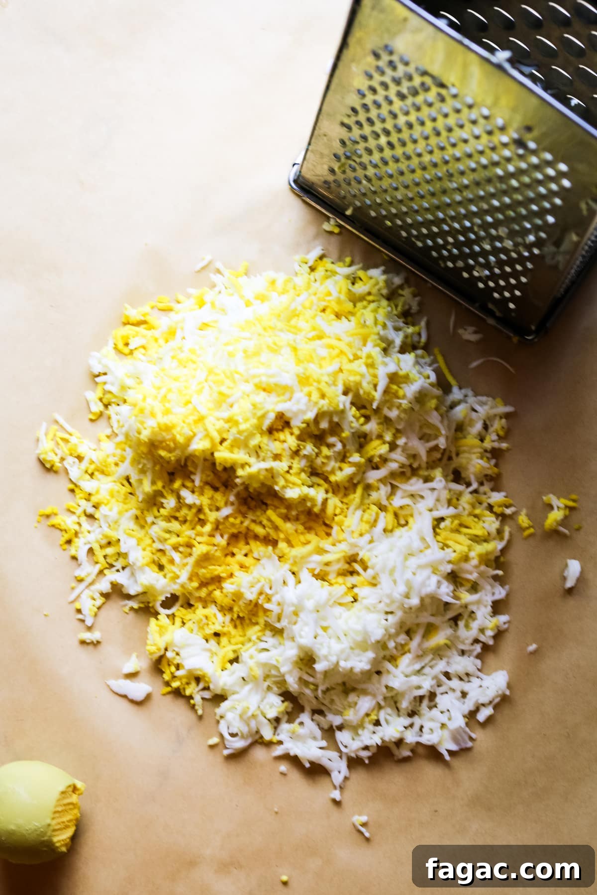 Cod Liver and Egg Salad Recipe: Creamy, Tangy Seafood Salad 7 shredded eggs on parchment paper with a box grater to the side.