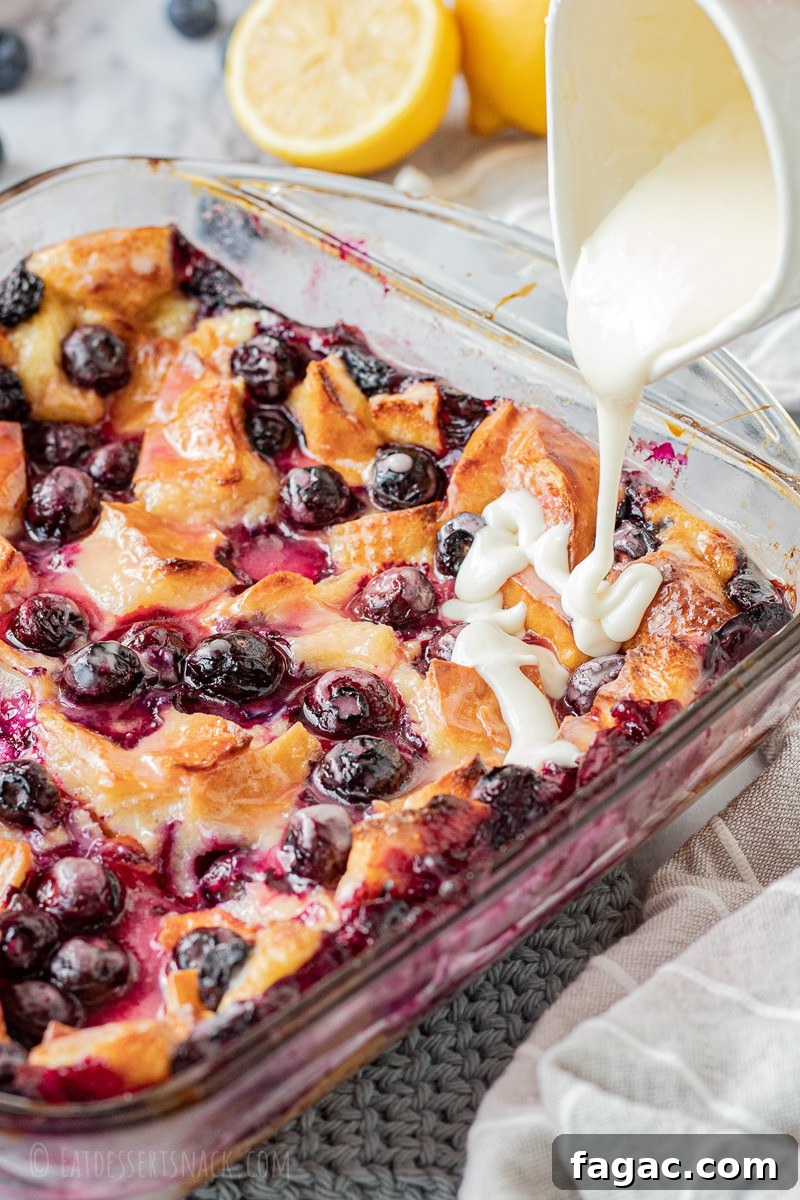 Baked lemon blueberry bread pudding in glass pan with lemon icing pouring on top.
