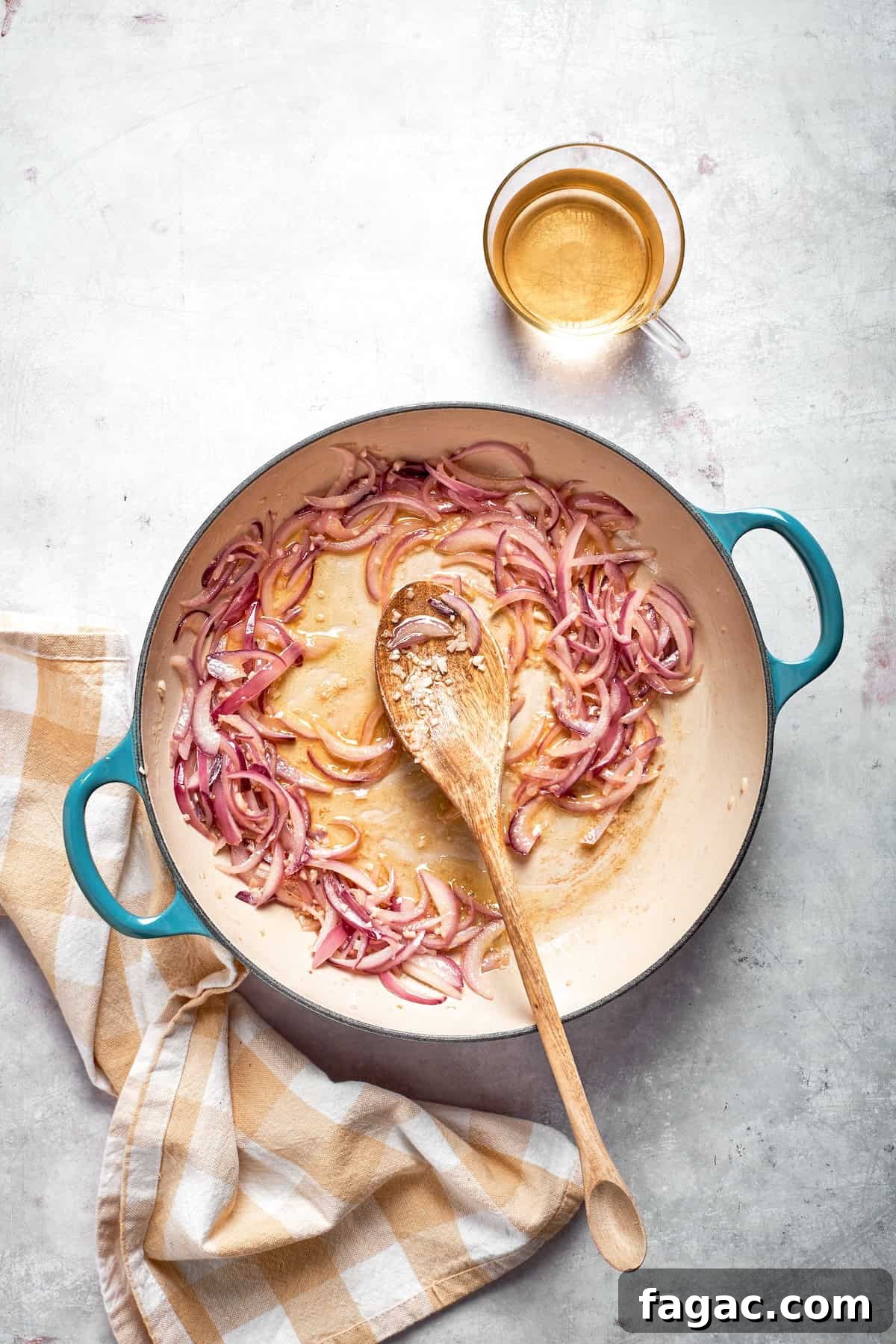 Sautee the onion and garlic. A spoon stirs a skillet of cooking onions and garlic.