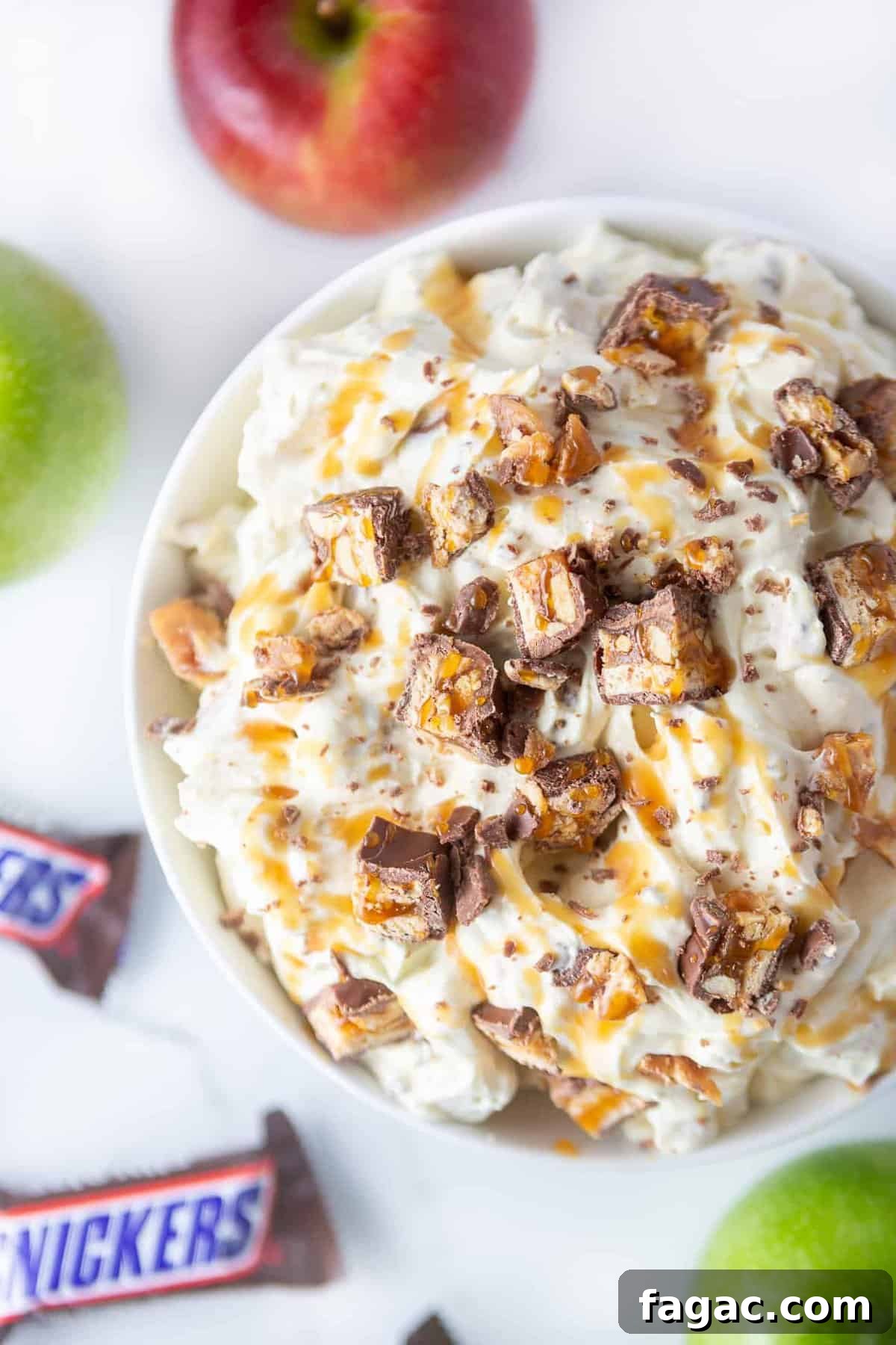 Apple Snickers Salad Recipe: Crunchy Caramel Apple Dessert Salad 2 White bowl of apple snickers salad. A fluffy vanilla pudding dessert topped with chopped snickers candy bars and caramel sauce.