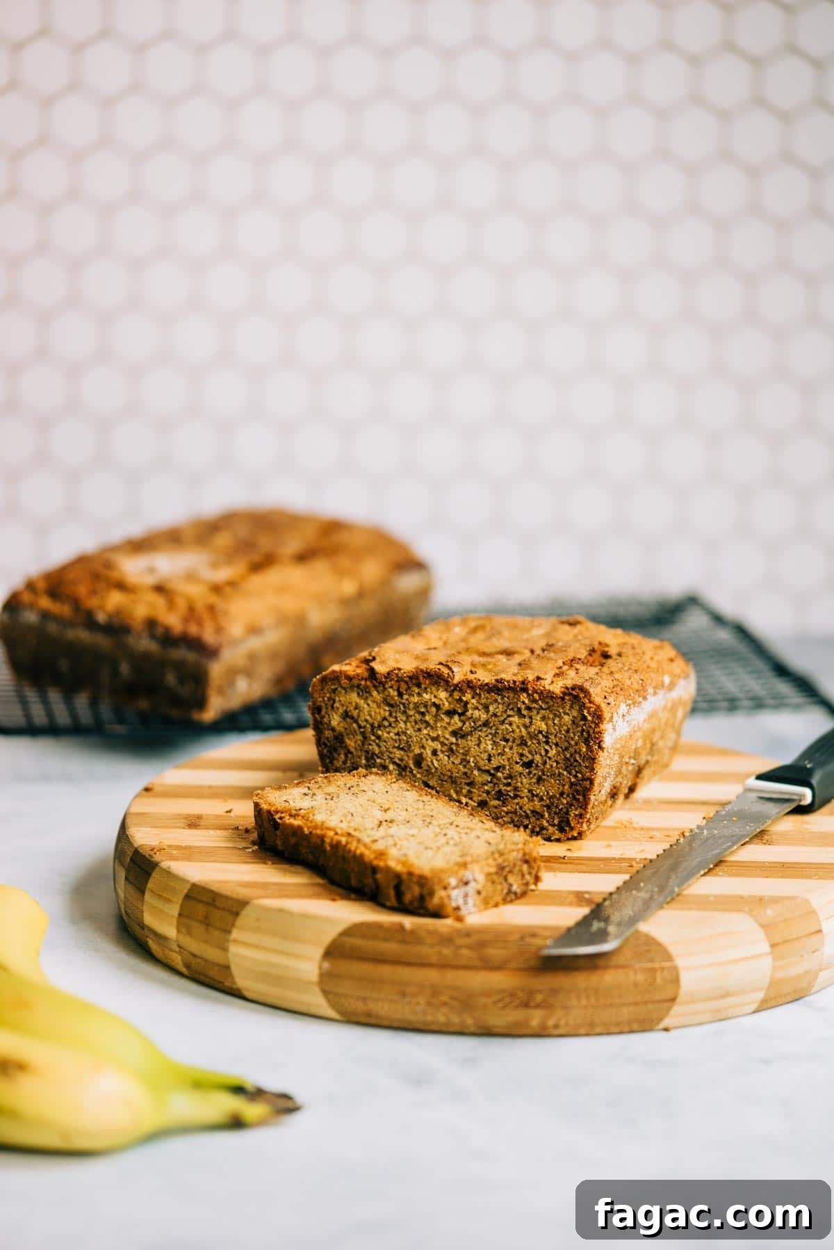 Crispy Sugar-Topped Banana Walnut Bread Recipe 5 A loaf of sliced banana bread on a striped cutting board with knife