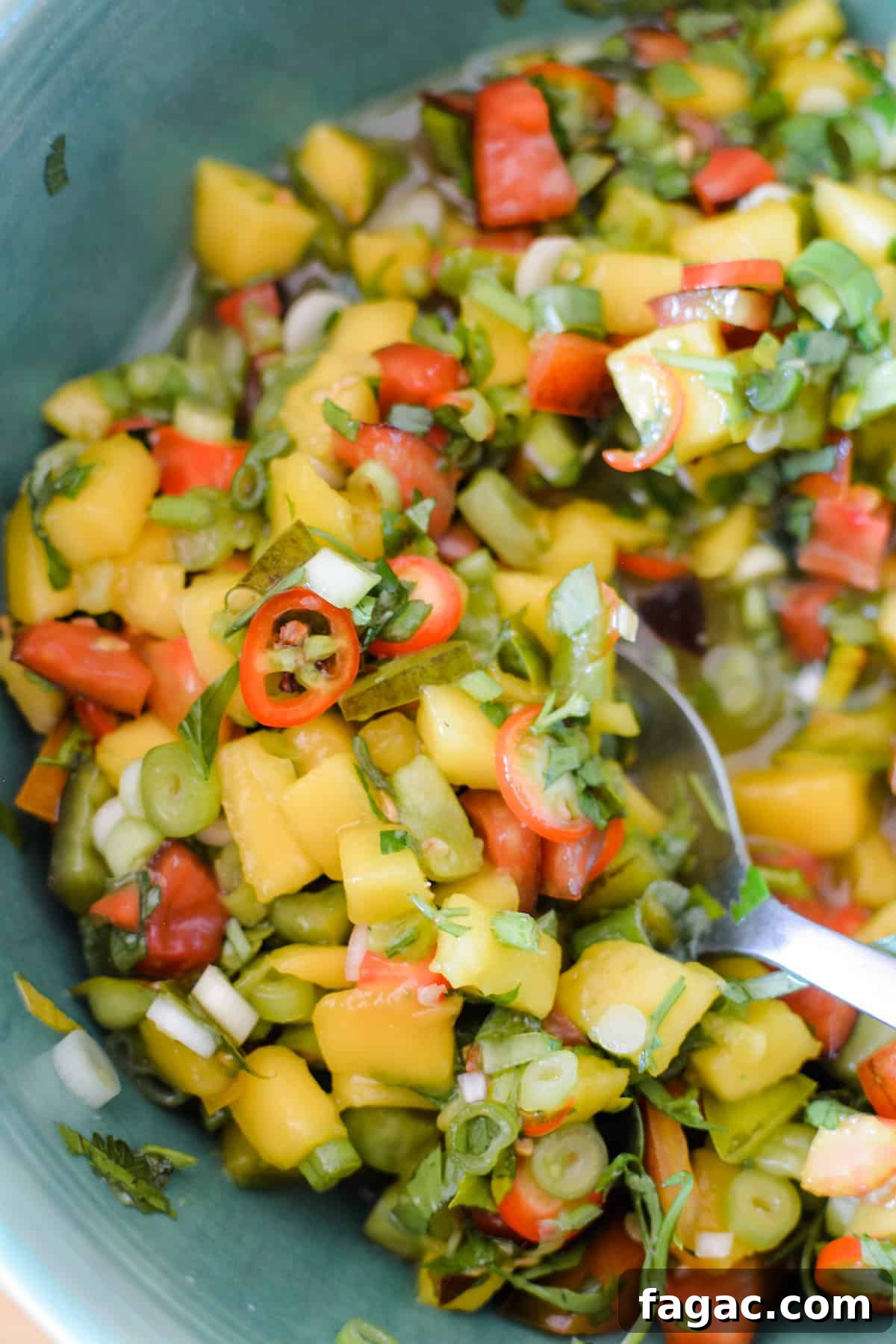 A close up of mango margarita salsa in a bowl with a spoon sticking in the salsa. 