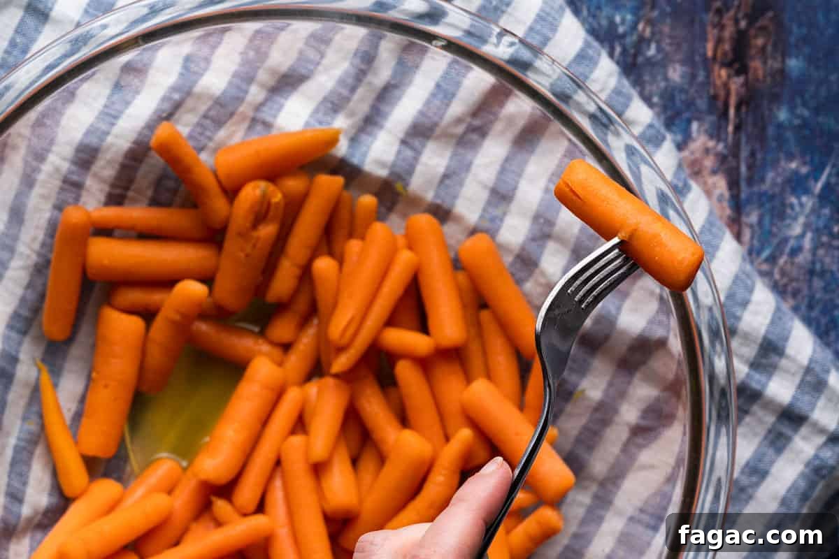 Honey-Glazed Orange Carrots with Citrus Butter Glaze 8 fork piercing cooked baby carrot overtop bowl of carrots