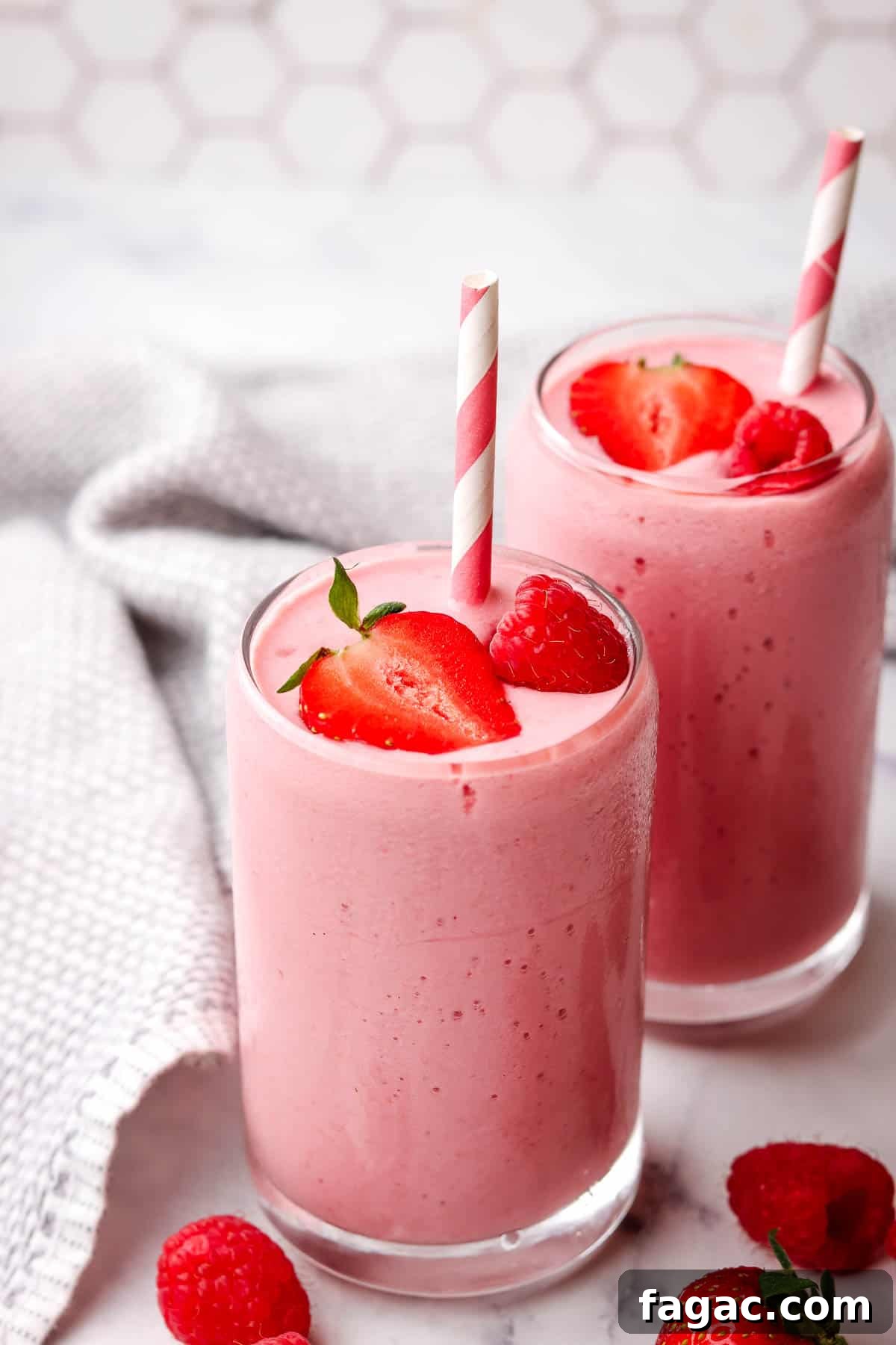 Creamy Strawberry Raspberry Smoothie Recipe for Spring Refreshment 2 Two pink strawberry raspberry smoothies garnished with berries and a paper straw.