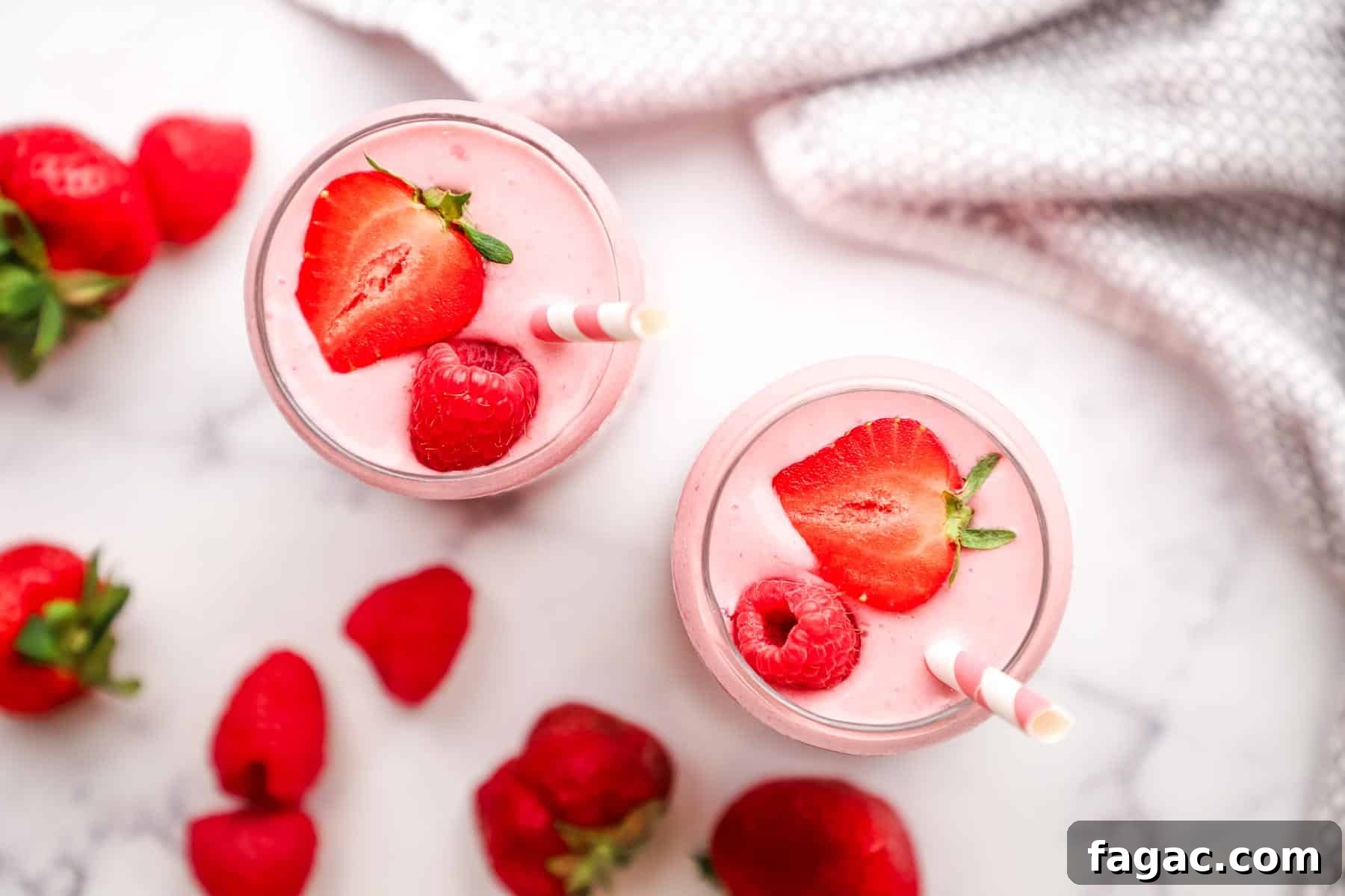 Creamy Strawberry Raspberry Smoothie Recipe for Spring Refreshment 3 overhead view of two glasses of strawberry raspberry smoothie topped with fresh strawberries and with pink straws in the glasses.