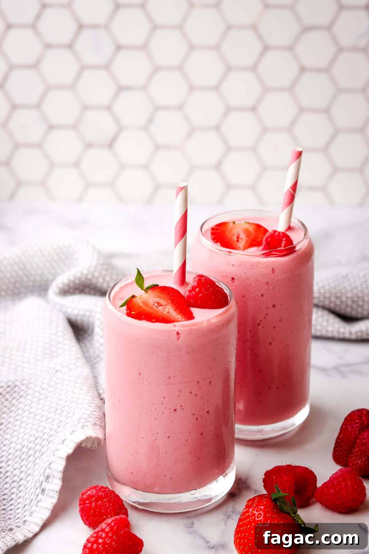 Creamy Strawberry Raspberry Smoothie Recipe for Spring Refreshment 7 Two pink strawberry raspberry smoothies garnished with berries and a paper straw.