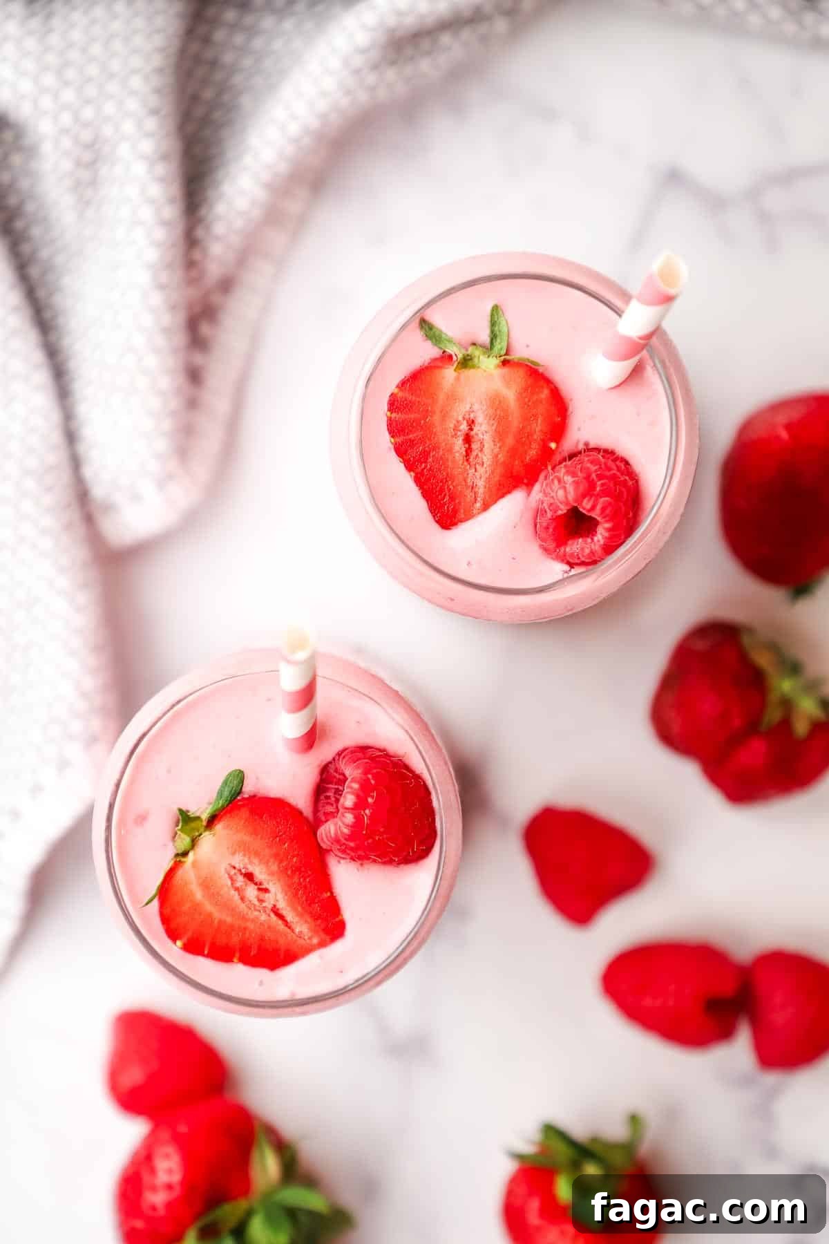 Creamy Strawberry Raspberry Smoothie Recipe for Spring Refreshment 8 overhead view of two glasses of strawberry raspberry smoothie topped with fresh strawberries and with pink straws in the glasses.