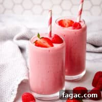 Two pink strawberry raspberry smoothies garnished with berries and a paper straw.