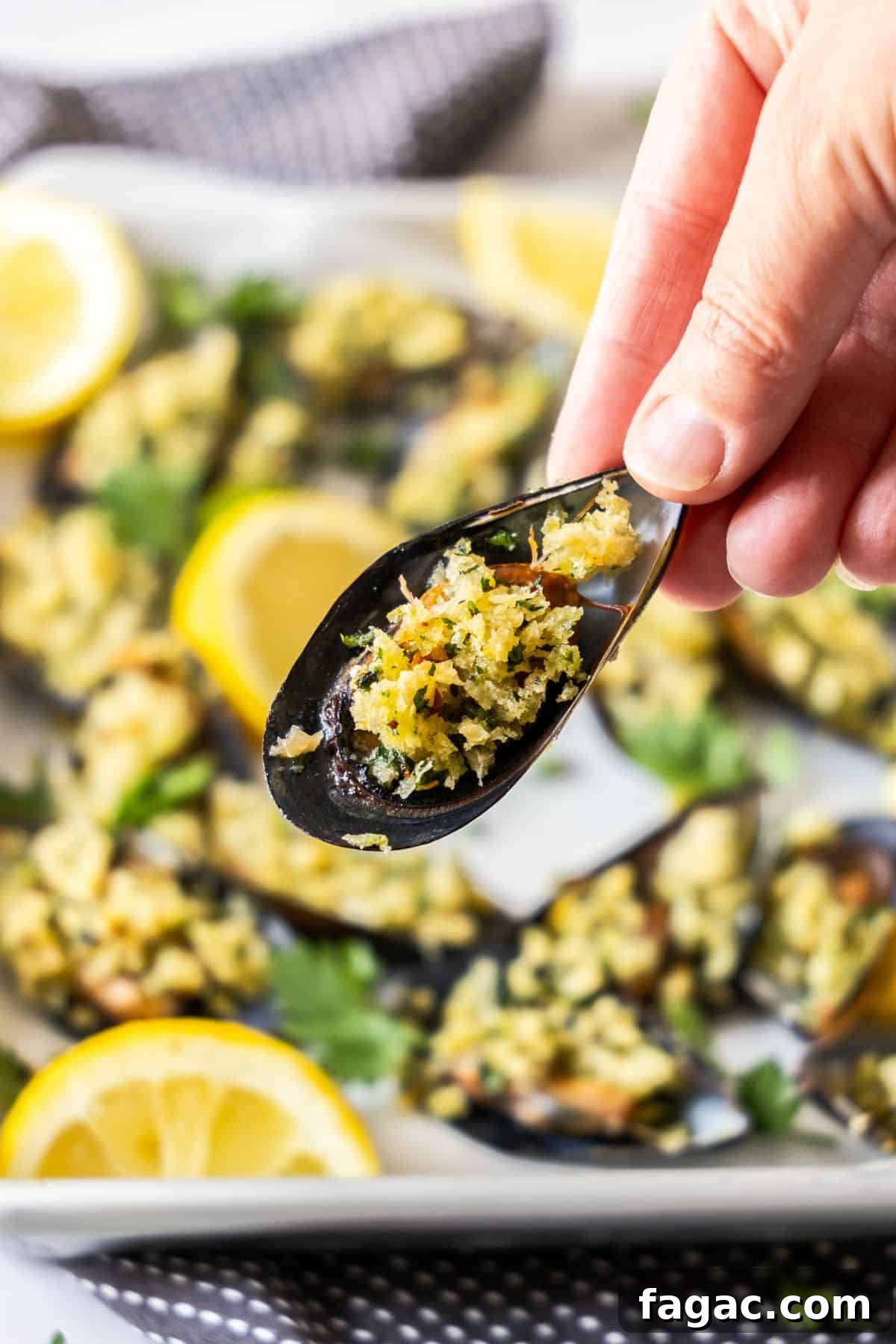 Hand holding up a Stuffed Mussel, with a tray of mussels in the background.