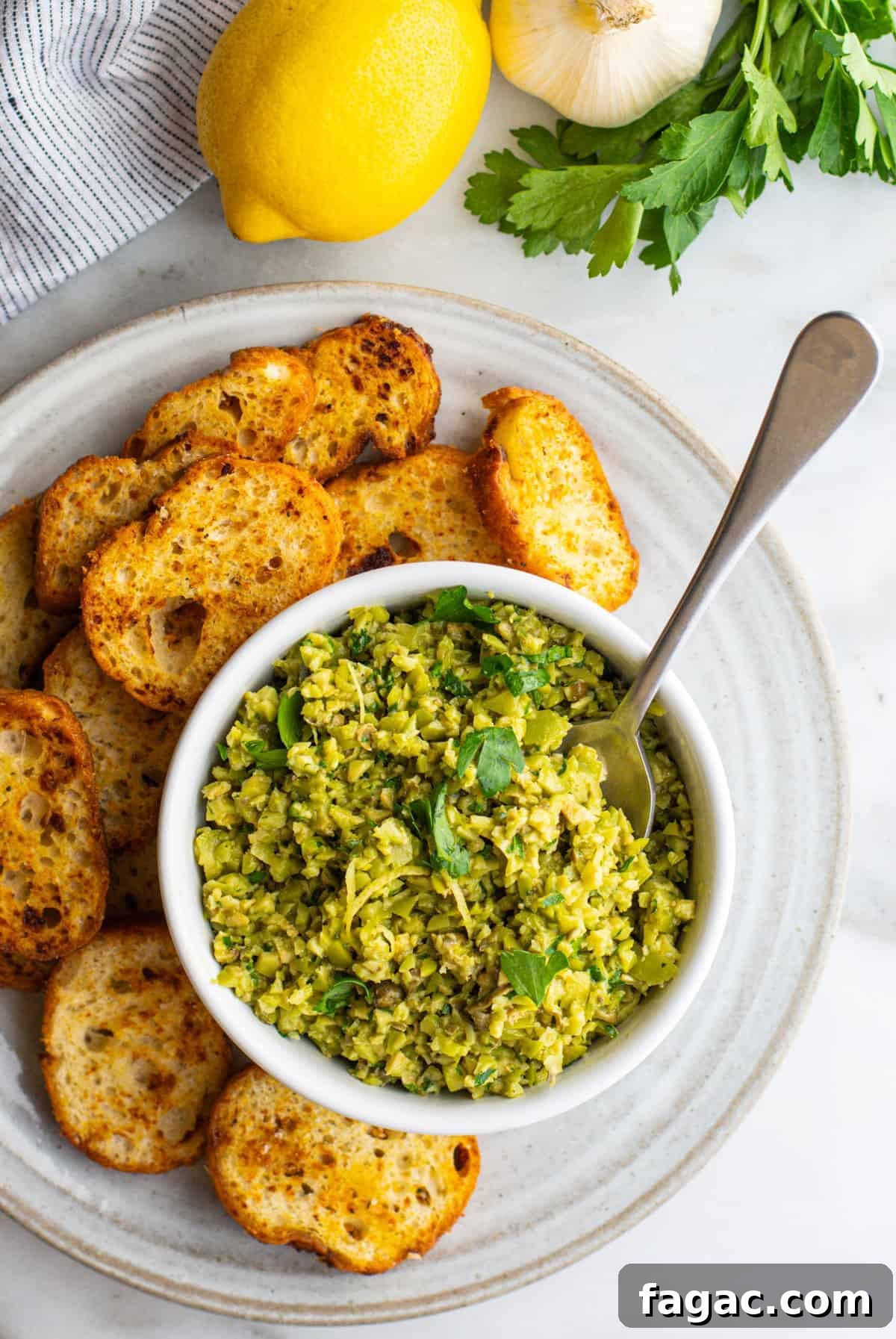 Green Olive Tapenade photographed from above served in a white bowl with crostini around.