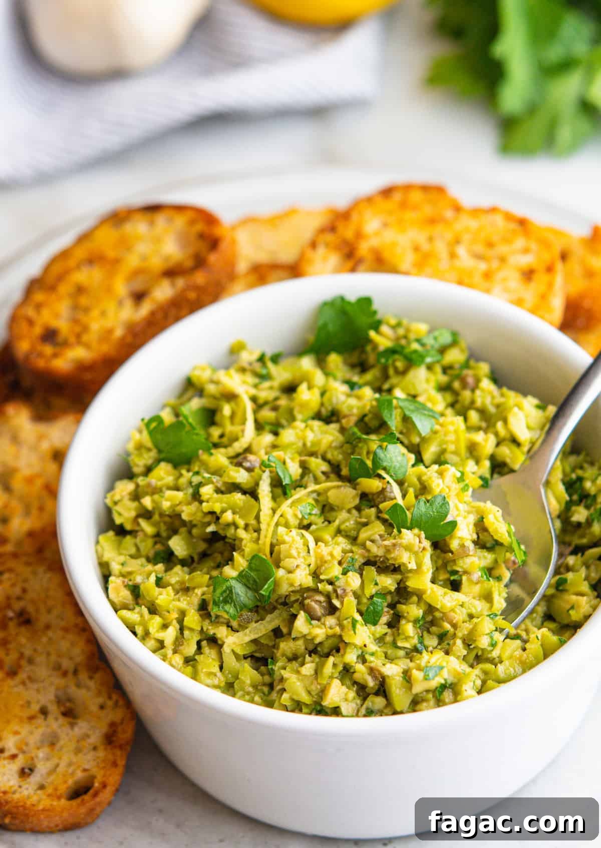 Green Olive Tapenade served in a white bowl with crostini around.