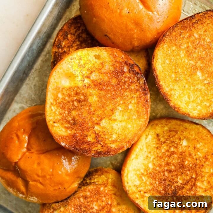 Up-close shot of golden toasted brioche burger buns on a baking sheet.