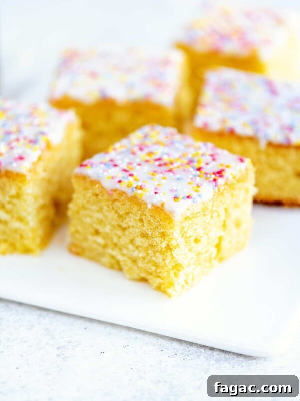 Slices of classic school vanilla sponge cake topped with white icing and colorful sprinkles