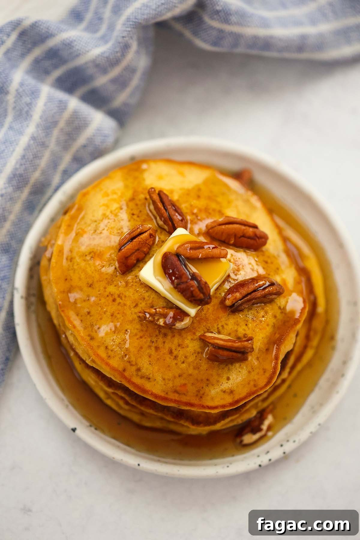 a stack of sweet potato pancakes with pecans, butter, and maple syrup.