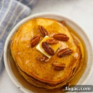 a stack of sweet potato pancakes with pecans, butter, and maple syrup.