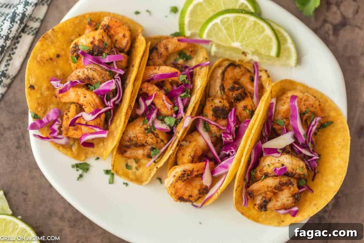 4 Shrimp Tacos in corn tortillas topped with red cabbage and chopped cilantro on a plate with a side of lime wedges.