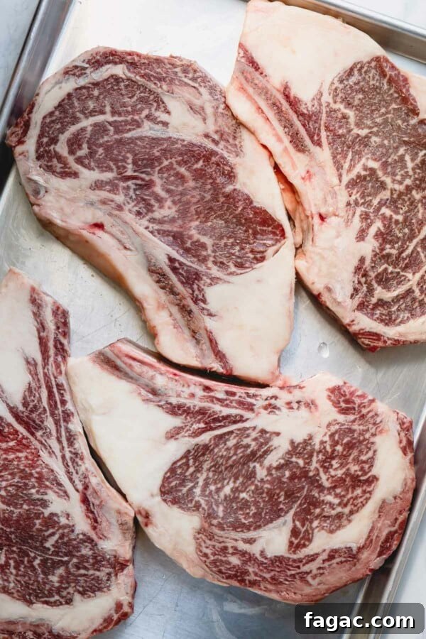 How to Grill a Tender, Flavorful Steak Every Time 4 4 raw ribeye steaks on a baking sheet.