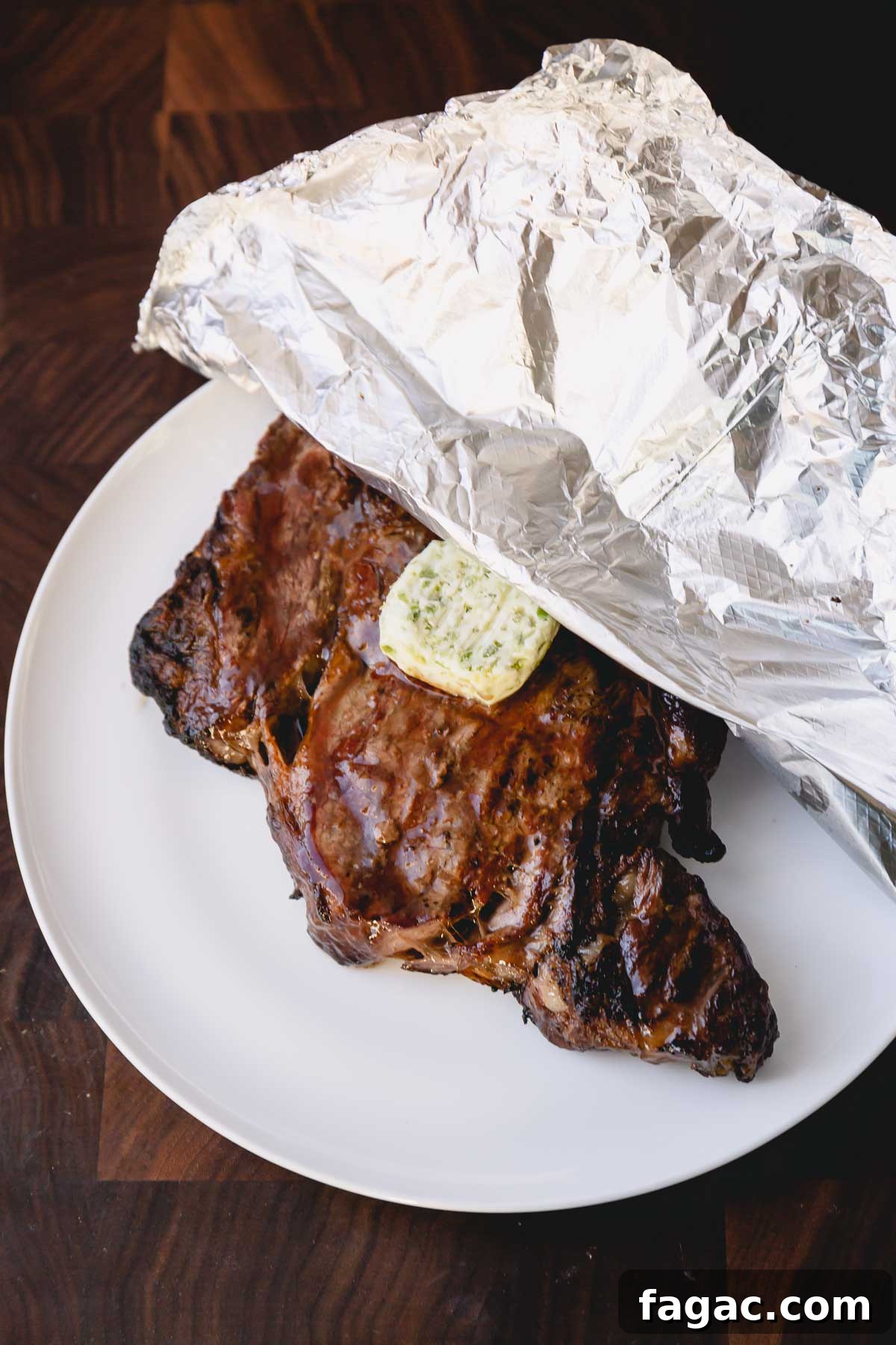 How to Grill a Tender, Flavorful Steak Every Time 10 Grilled ribeye steak with a slice of compound butter on a plate half covered with foil