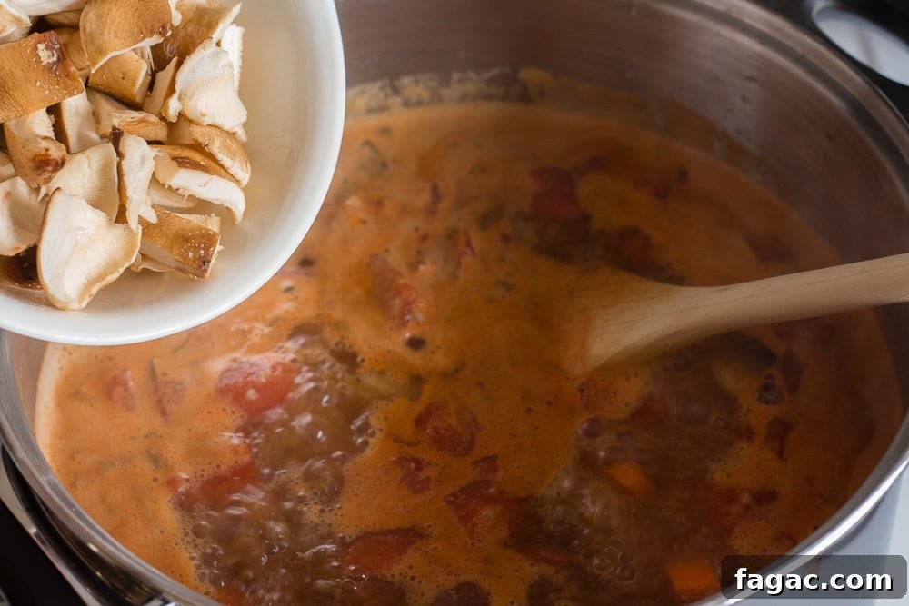 Cut up mushrooms in a white bowl being put into a pot of soup on the stove. A wooden spoon rests in the soup.