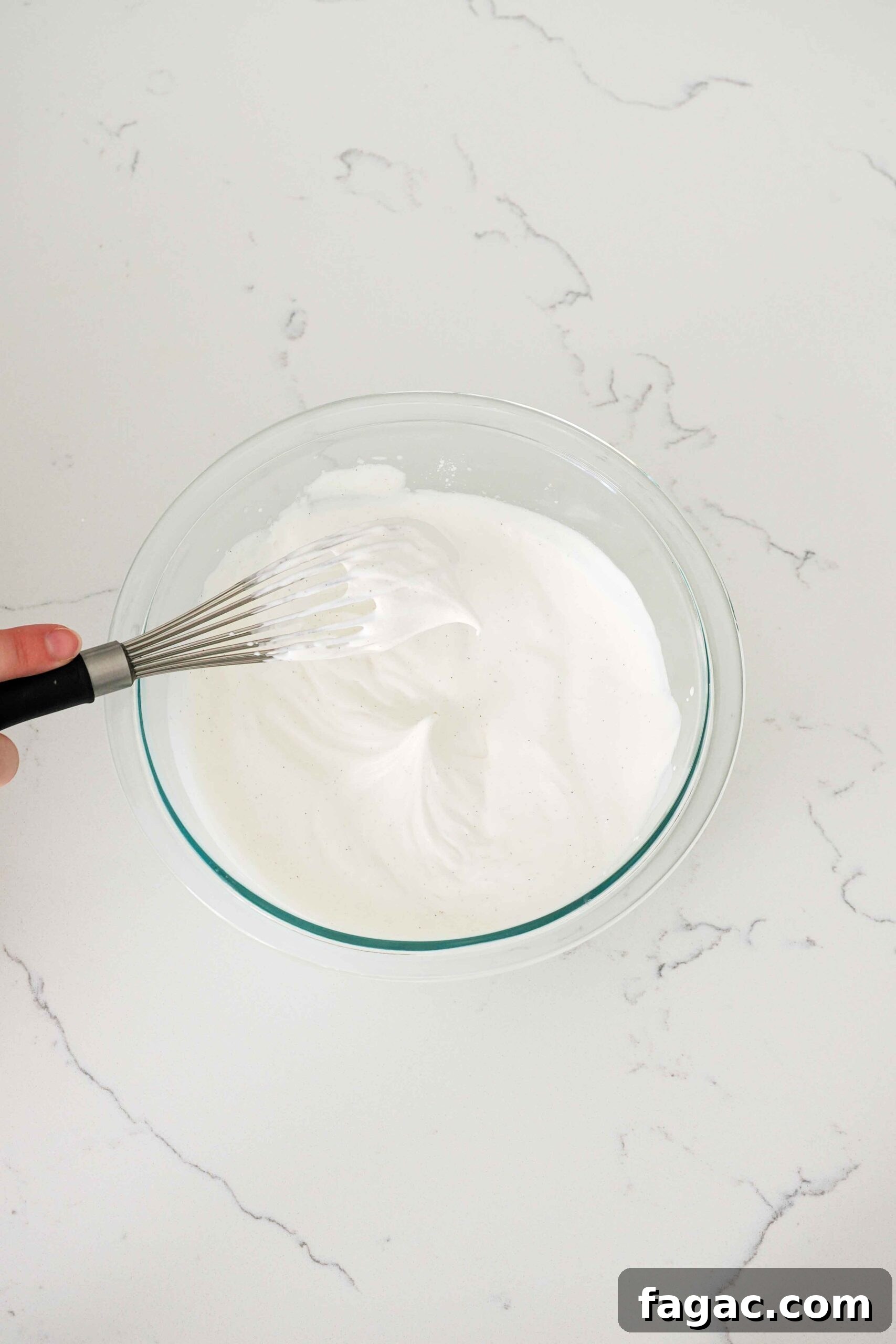 Silky Vanilla Whipped Cream Recipe for Desserts and Toppings 5 A whisk with a clump of whipped cream drooping off of it in soft peaks.