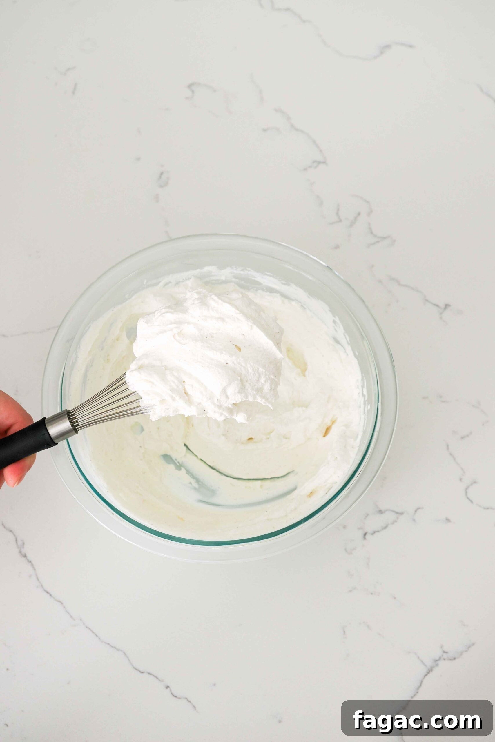 Silky Vanilla Whipped Cream Recipe for Desserts and Toppings 6 A whisk holds up a clump of whipped cream with stiff peaks.