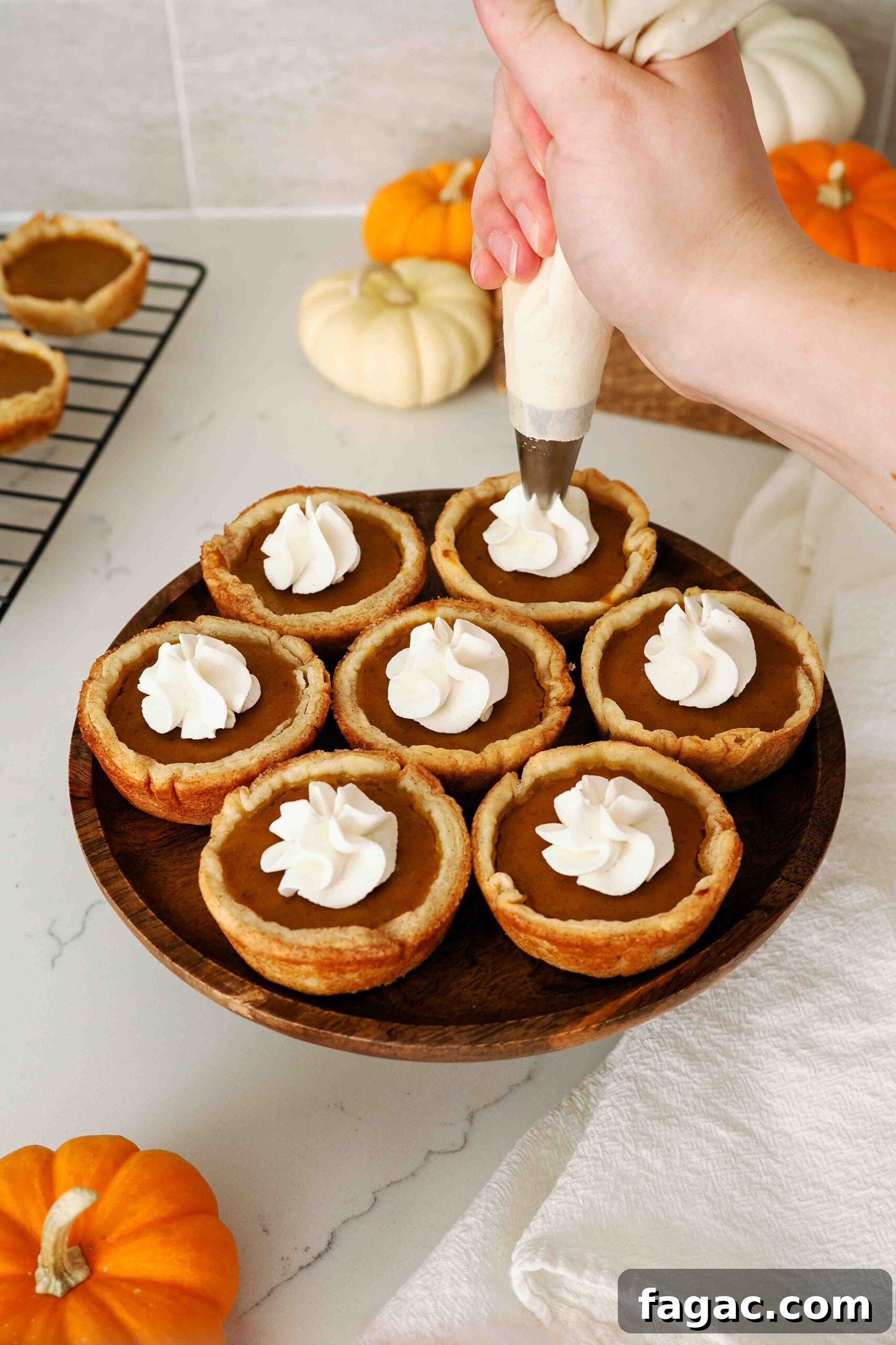 Silky Vanilla Whipped Cream Recipe for Desserts and Toppings 9 A hand pipes a dollop of whipped cream onto individual pumpkin pies.