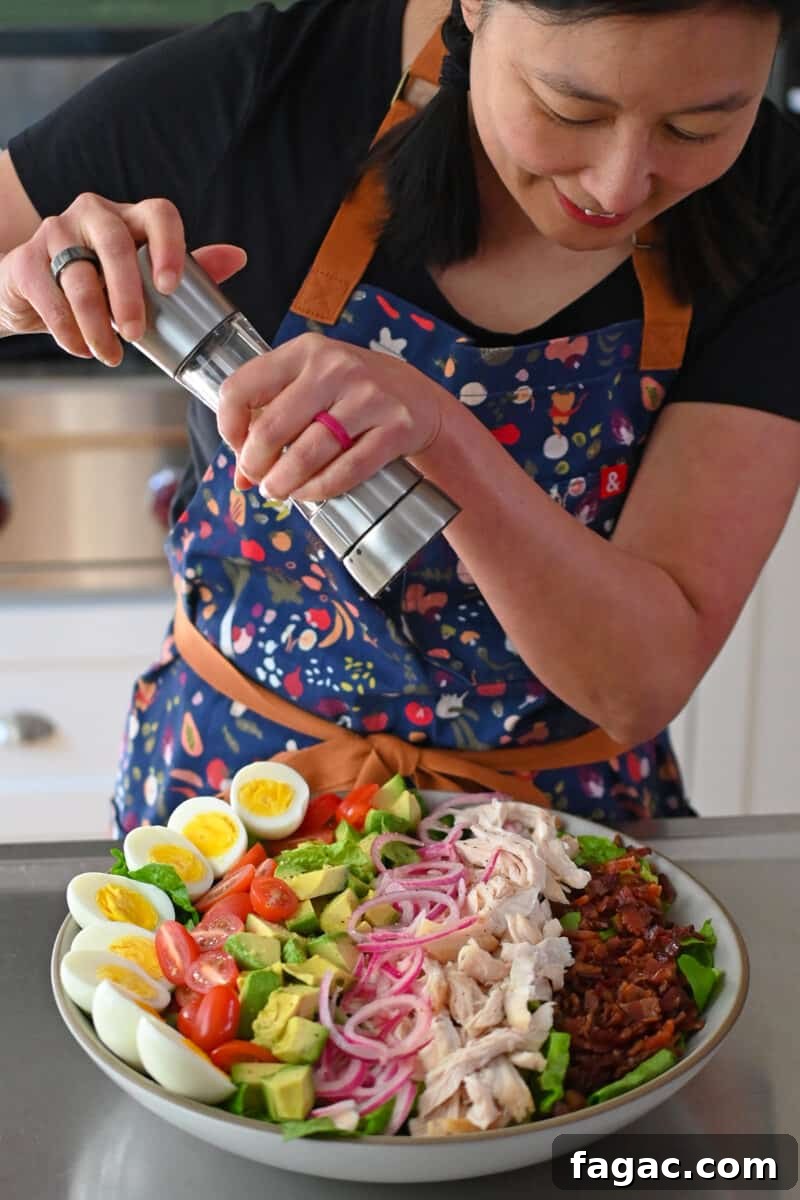 An Asian woman is grinding fresh black pepper on top of a Green Goddess Cobb Salad,