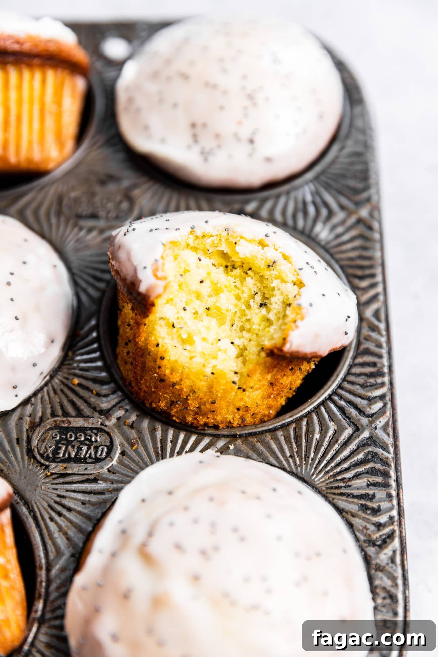 Close up of lemon poppy seed muffins in muffin pan with a bite missing from one.