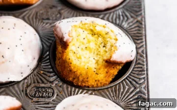Lemon Poppy Seed Muffins in a muffin tin with a bite missing from one muffin