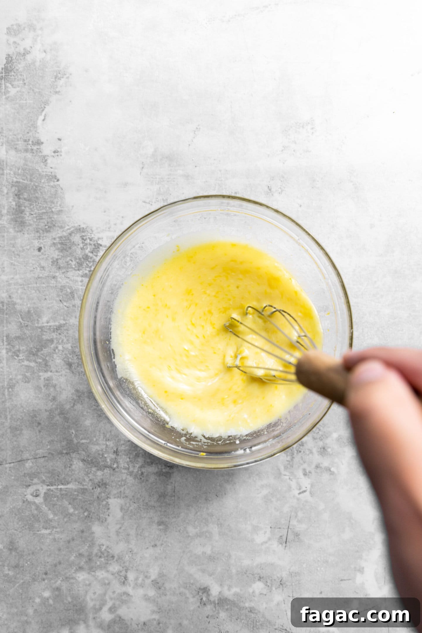 Lemon zest, sugar, oil, egg, yogurt, sour cream, milk, and lemon juice being whisked together.