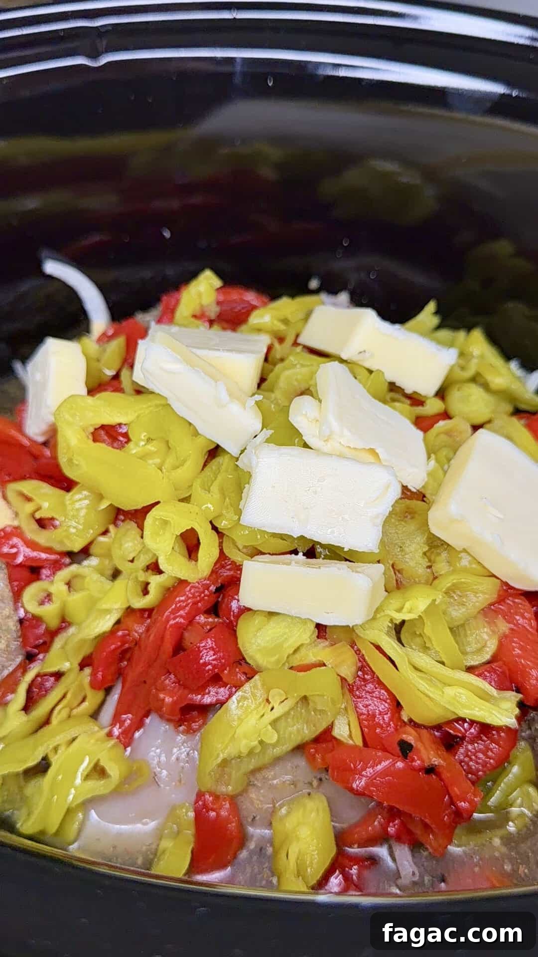 Crockpot Chicken Philly Cheesesteak Recipe for Slow-Cooked Sandwiches 8 Sliced yellow peppers, red peppers, and several pats of butter are layered on top of meat and onions inside a black slow cooker.