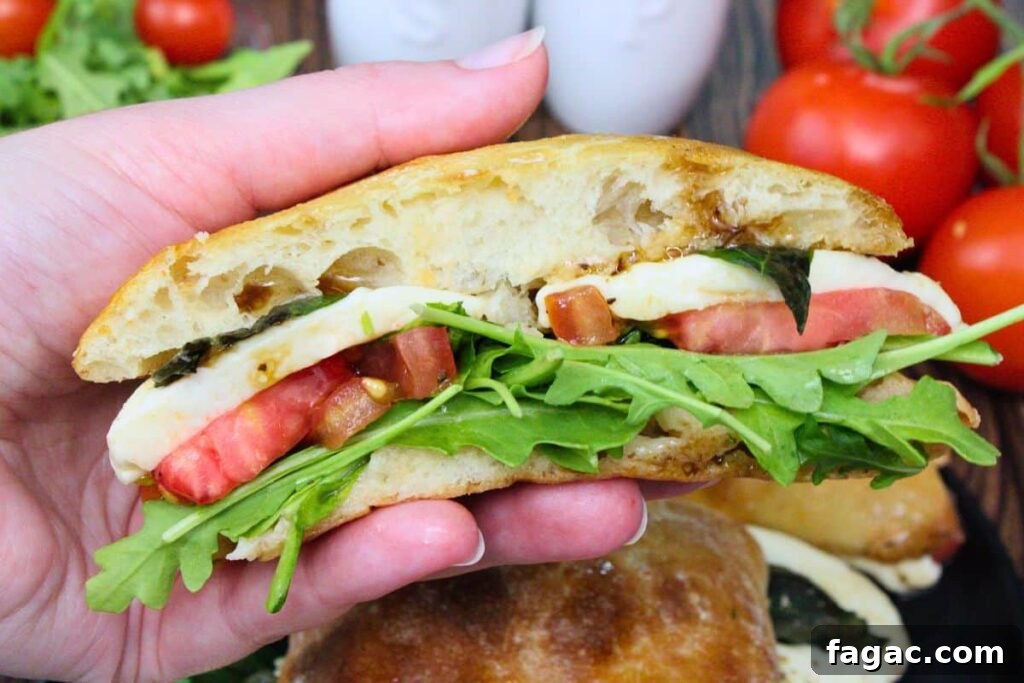 holding up half of an air fryer caprese sandwich showing off the tomato, mozzarella cheese, and arugula