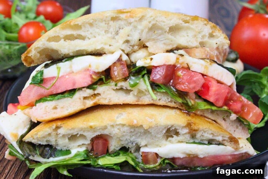 two halves of caprese sandwich stacked on top of each other showing tomatoes mozzarella cheese and fresh greens