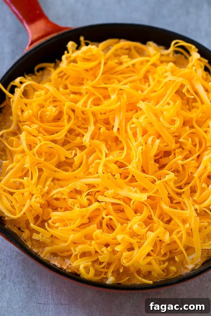 Buffalo Ranch Chicken Dip Buffalo chicken dip topped with shredded cheddar cheese, ready to go into the oven.