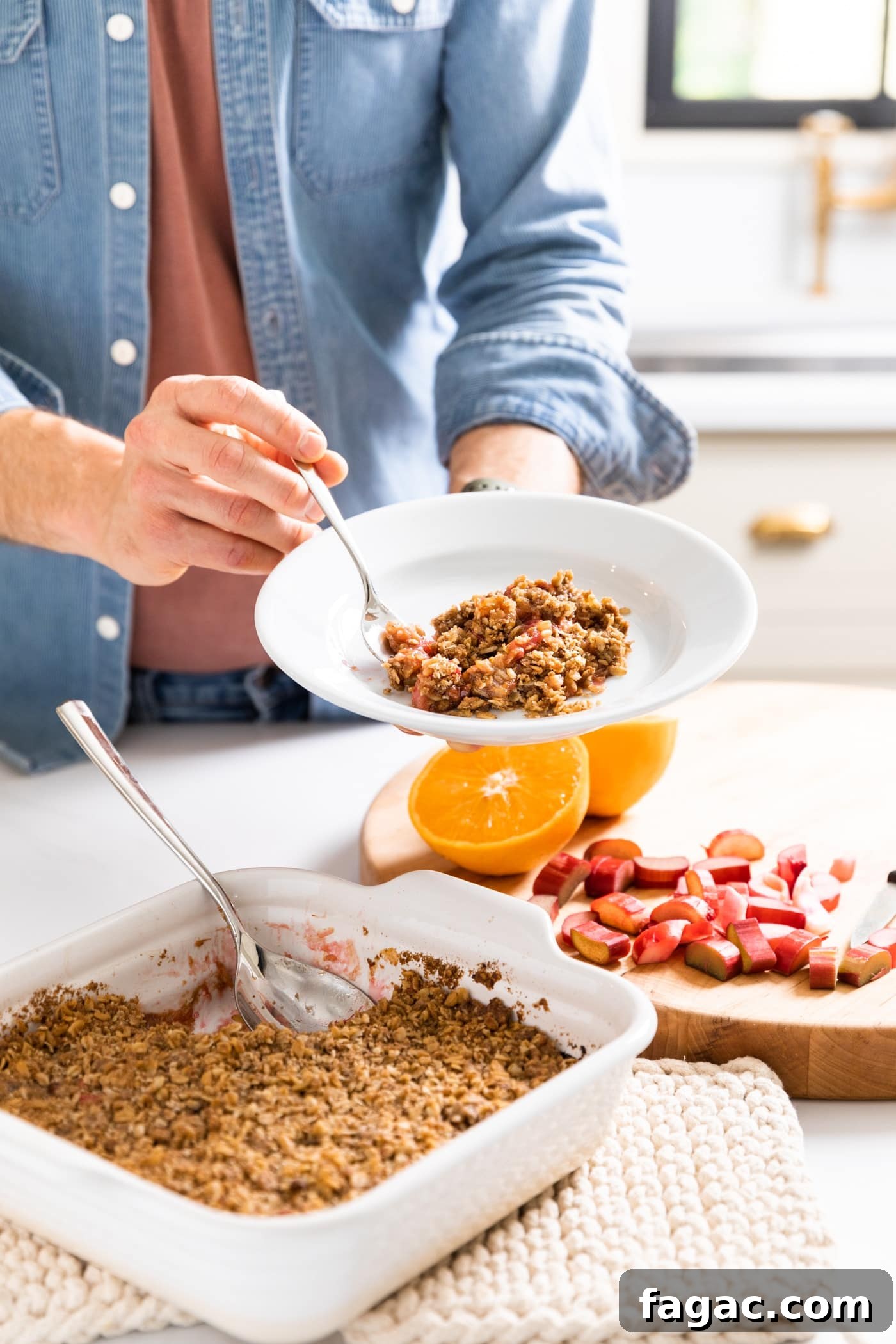 Classic Rhubarb Crisp Recipe with Buttery Oat Topping 5 Man with blue shirt holding white plate with scoop of rhubarb crisp taken out of pan below with extra cut rhubarb in background